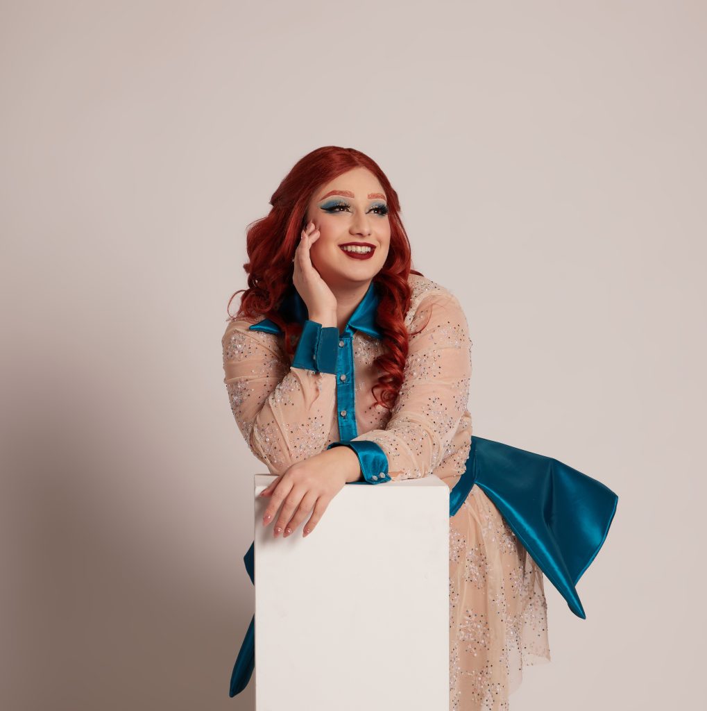 Image of Empress Alter posing photo a photo, leaning on a white column, featuring her signature red hair.